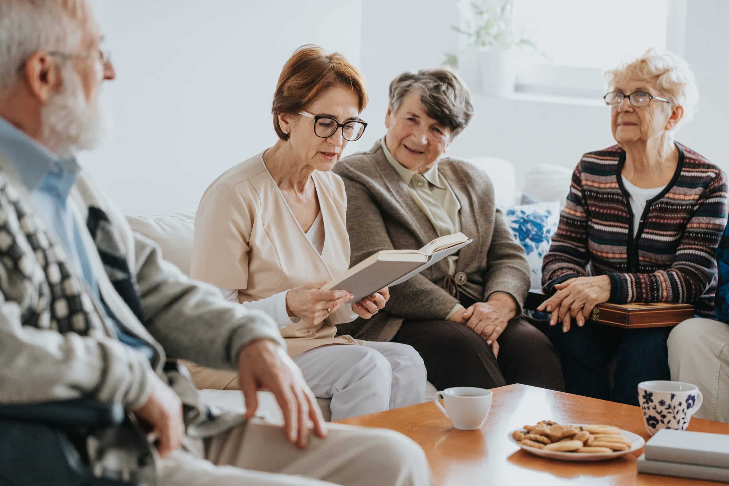 Helpful caregiver reading a book to a group of older people