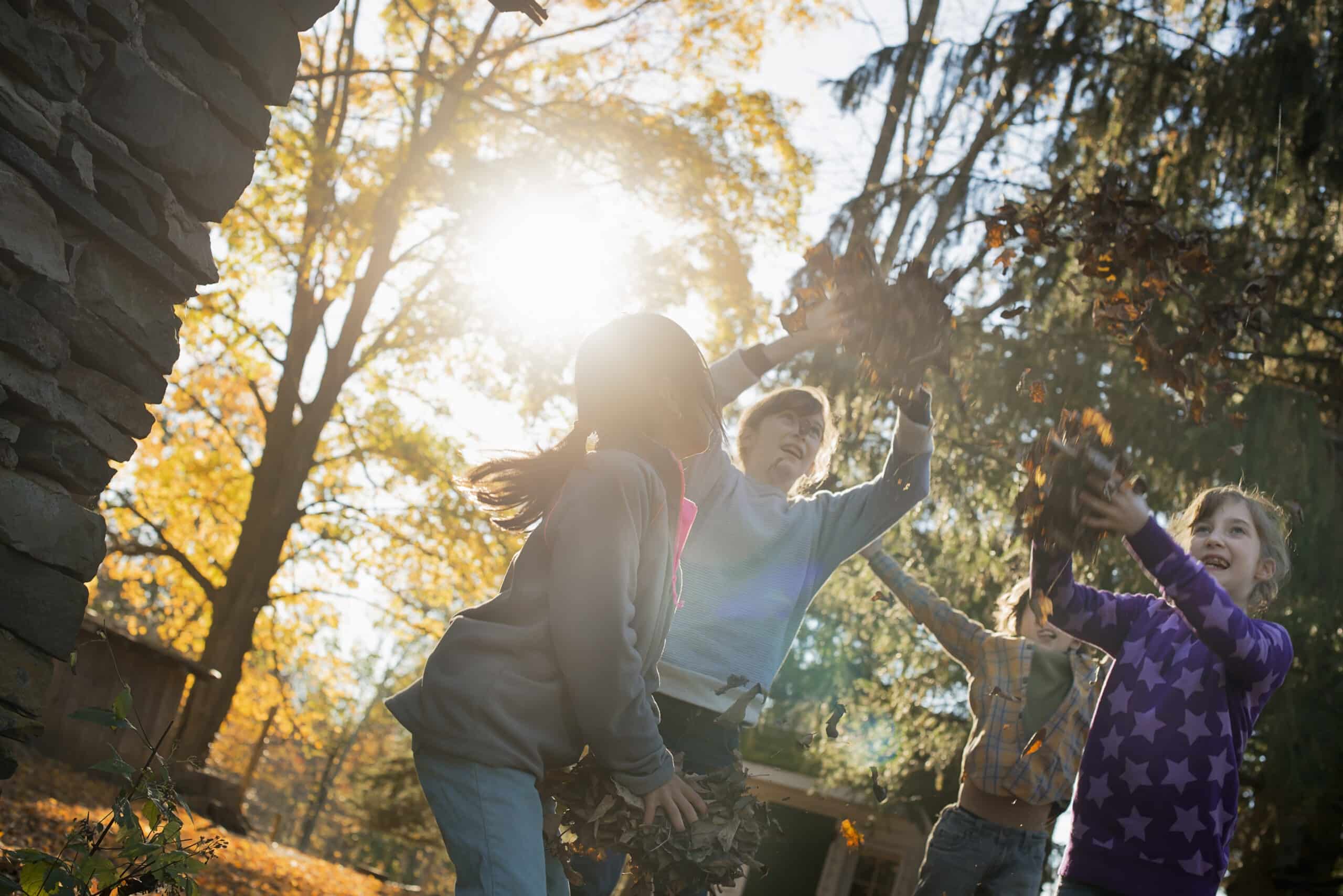 Three children in the autumn sunshine. Playing outdoors throwing the fallen leaves in the air.