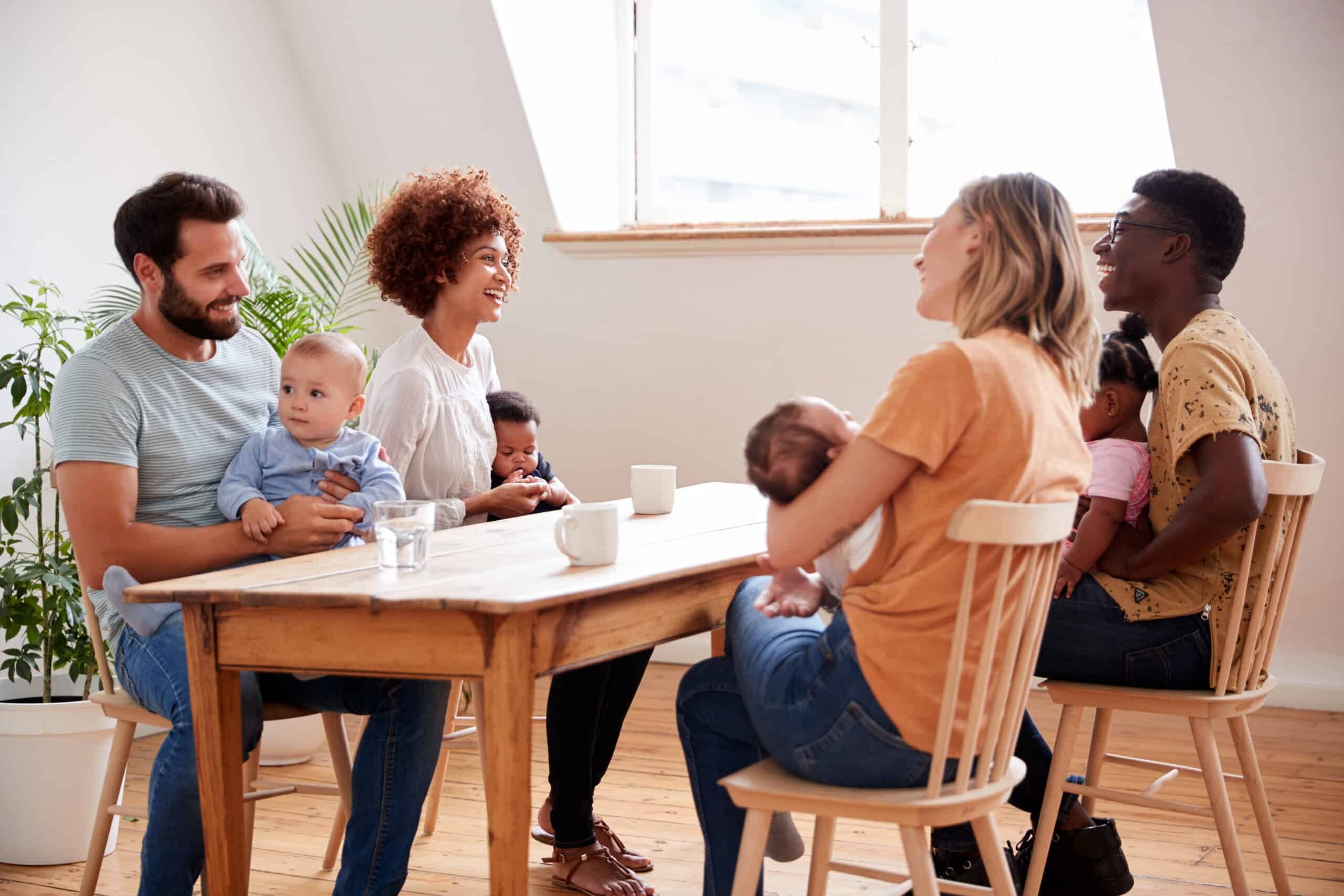 Two Families With Babies Meeting And Talking Around Table.