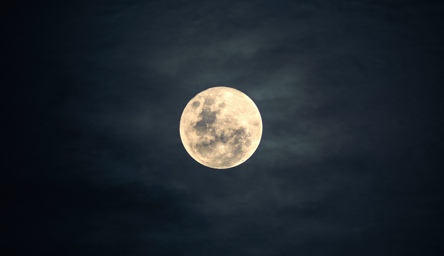 A Full Moon against a dark, slightly cloudy sky